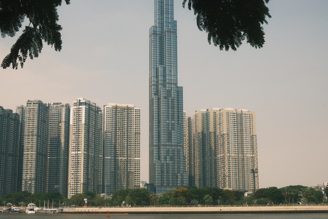 Modern skyscrapers rise above a tree-lined waterfront.