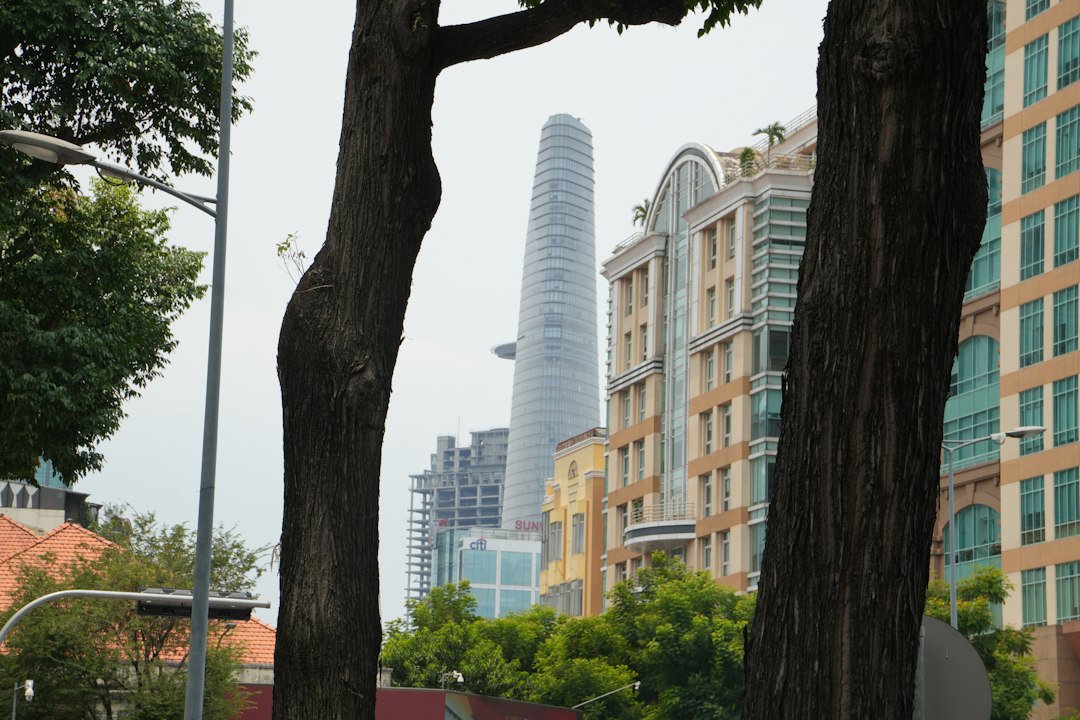 A tall skyscraper rises above city buildings and trees