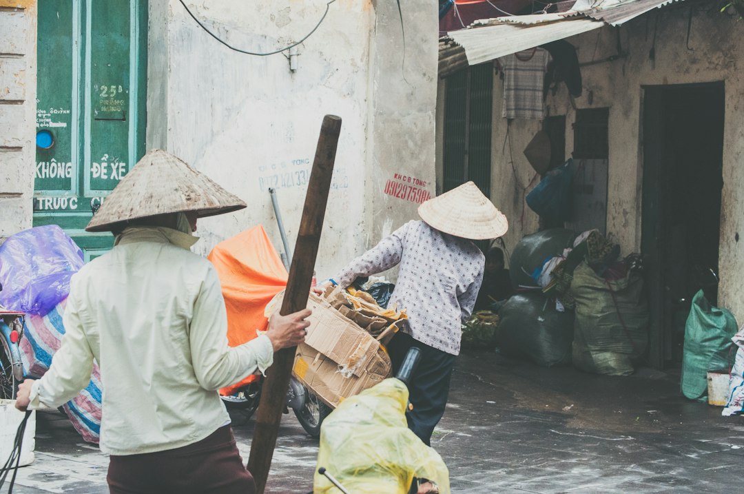 Two people in conical hats carrying cardboard and wood on a street in Hanoi